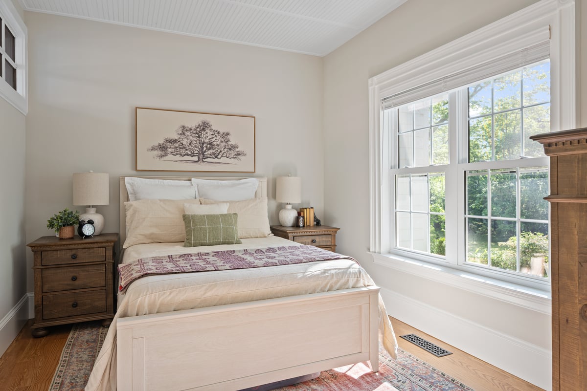Cozy bedroom inside a Norcross, GA, home with neutral bedding, matching wood nightstands, tree artwork, and large windows filling the room with natural light.