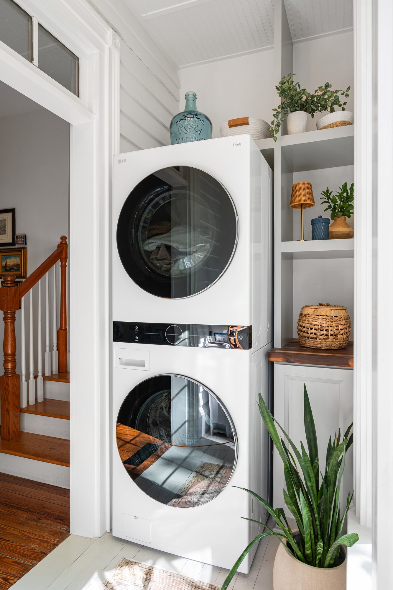 Compact laundry area inside a Norcross, GA, home with a stacked white washer and dryer beside built-in shelving, warm wood accents, woven baskets, and potted plants.