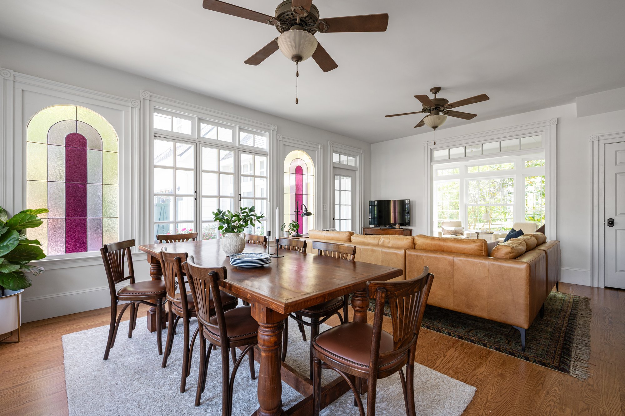 Open dining and living room inside a Norcross, GA, home with a large wood table, leather sectional, arched stained-glass windows, and abundant natural light.