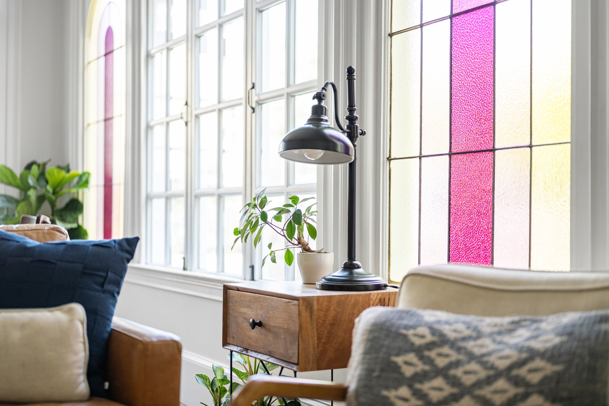 Cozy seating area inside a Norcross, GA, home with a wood side table, black reading lamp, potted plant, and colorful arched stained-glass windows.
