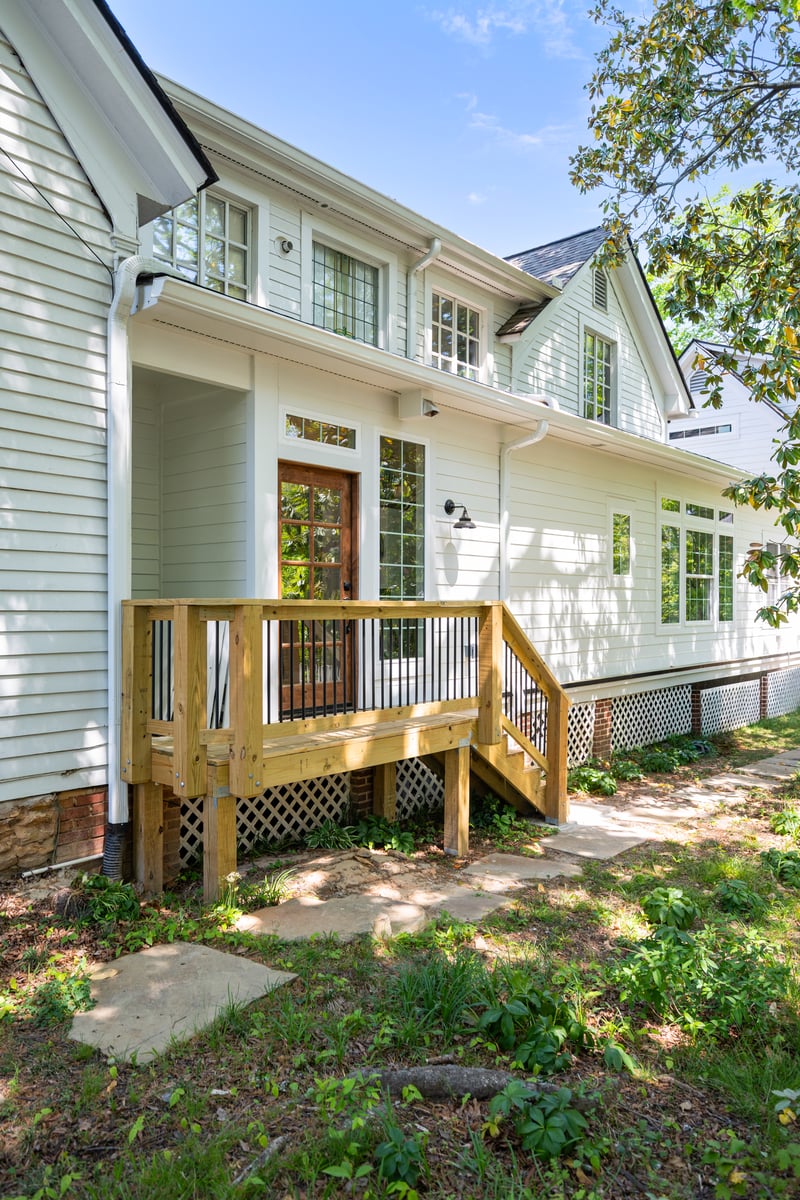 Rear exterior of a white two-story home addition in Norcross, GA, with large windows, a wood entry landing, black railings, and a garden path.