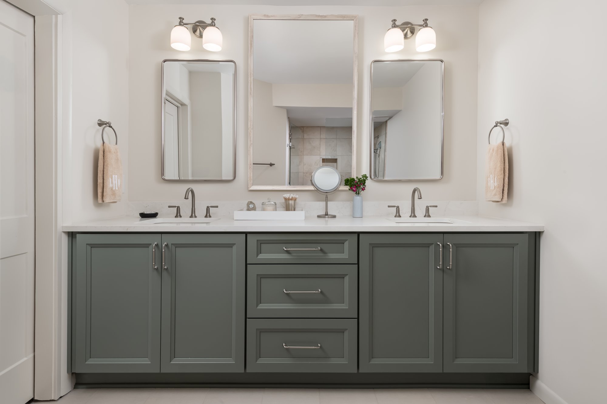 Image of a his-and-hers bathroom vanity in a Atlanta, Georgia, condo with light green cabinets, porcelain counters, and light fixtures over the mirrors.