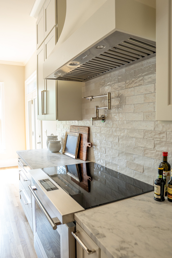 Sleek range with minimalist marble backsplash and modern pot filler by Exodus Design Build in Sugar Hill, GA