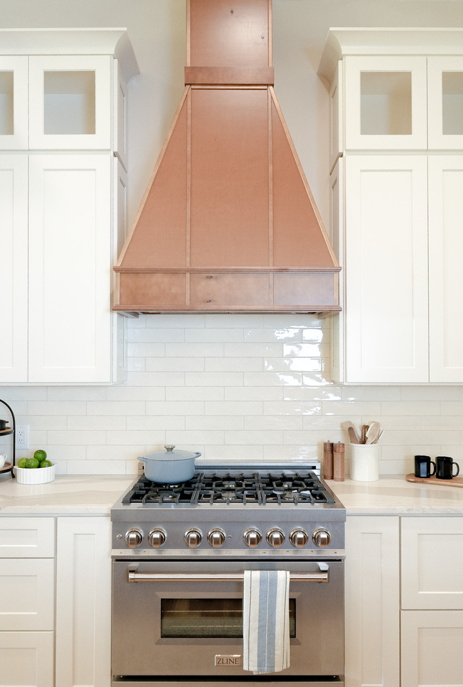 Straight-on view of copper vent hood and tile backsplash in modern kitchen by Exodus Design Build in Walnut Grove, GA