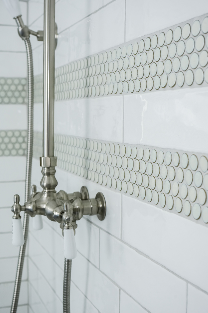 Detailed view of custom tilework and shower hardware in a bathroom by Exodus Design Build in Sugar Hill, GA.