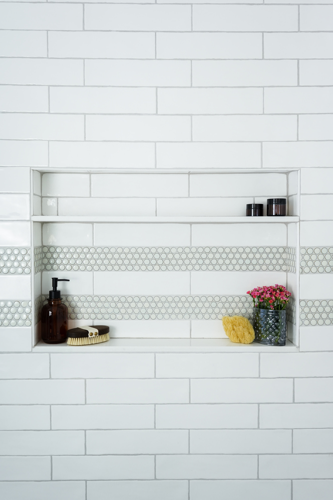 Shower niche with flowers, soap, and modern finishes in a bathroom by Exodus Design Build in Stone Mountain, GA.