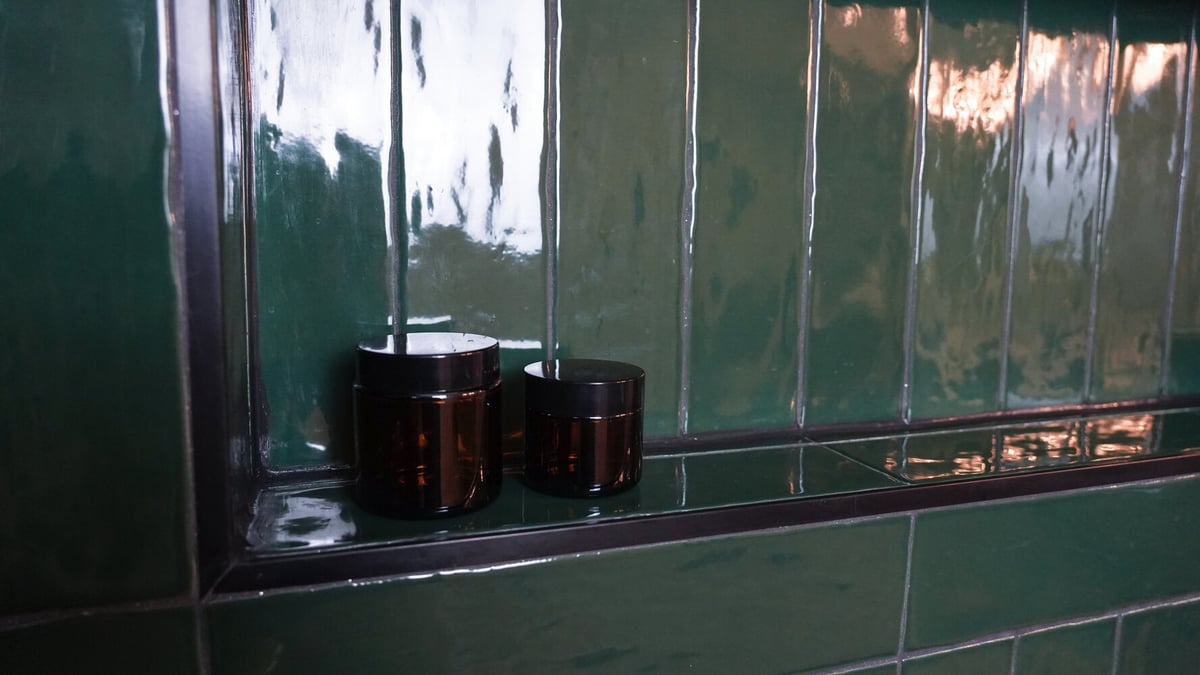 Close-up of amber jars on a green tiled niche in a custom shower by Exodus Design Build in Loganville, GA.