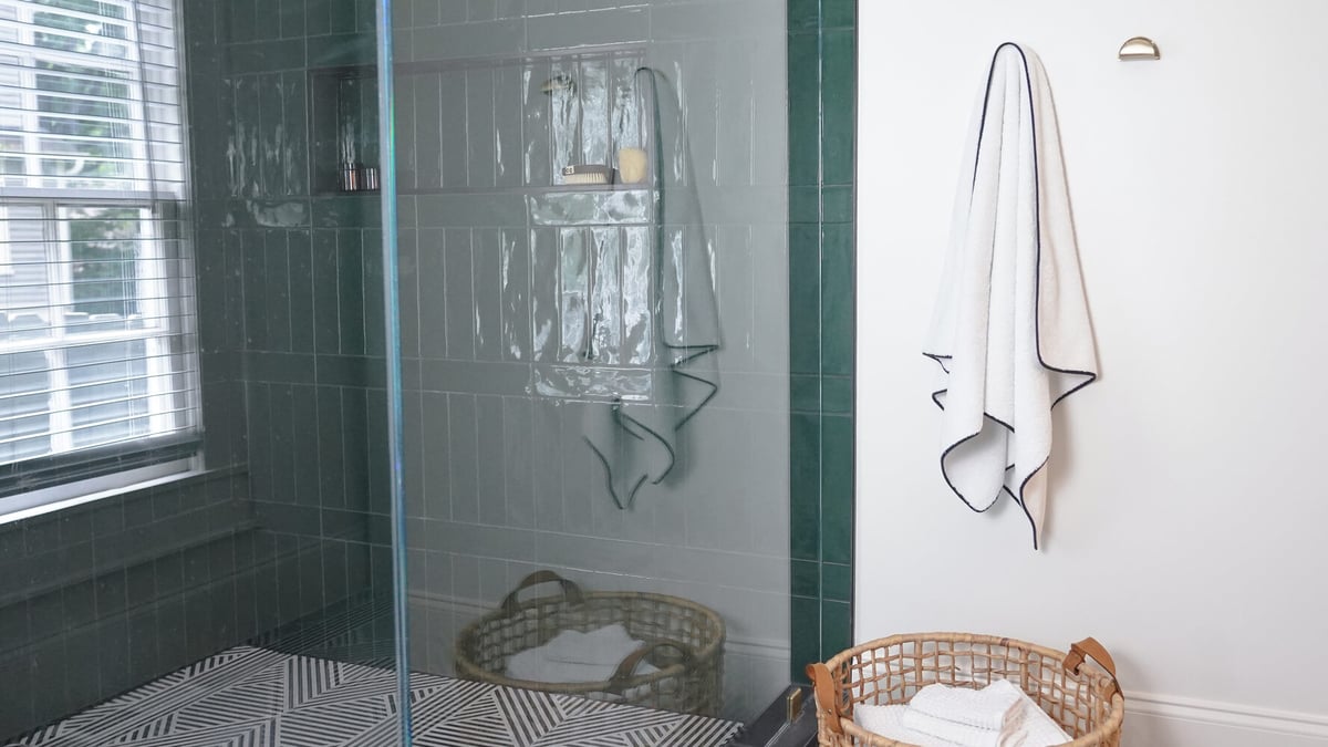 Luxury shower with emerald green tile, glass door, and white towel accent by Exodus Design Build in Gainesville, GA.