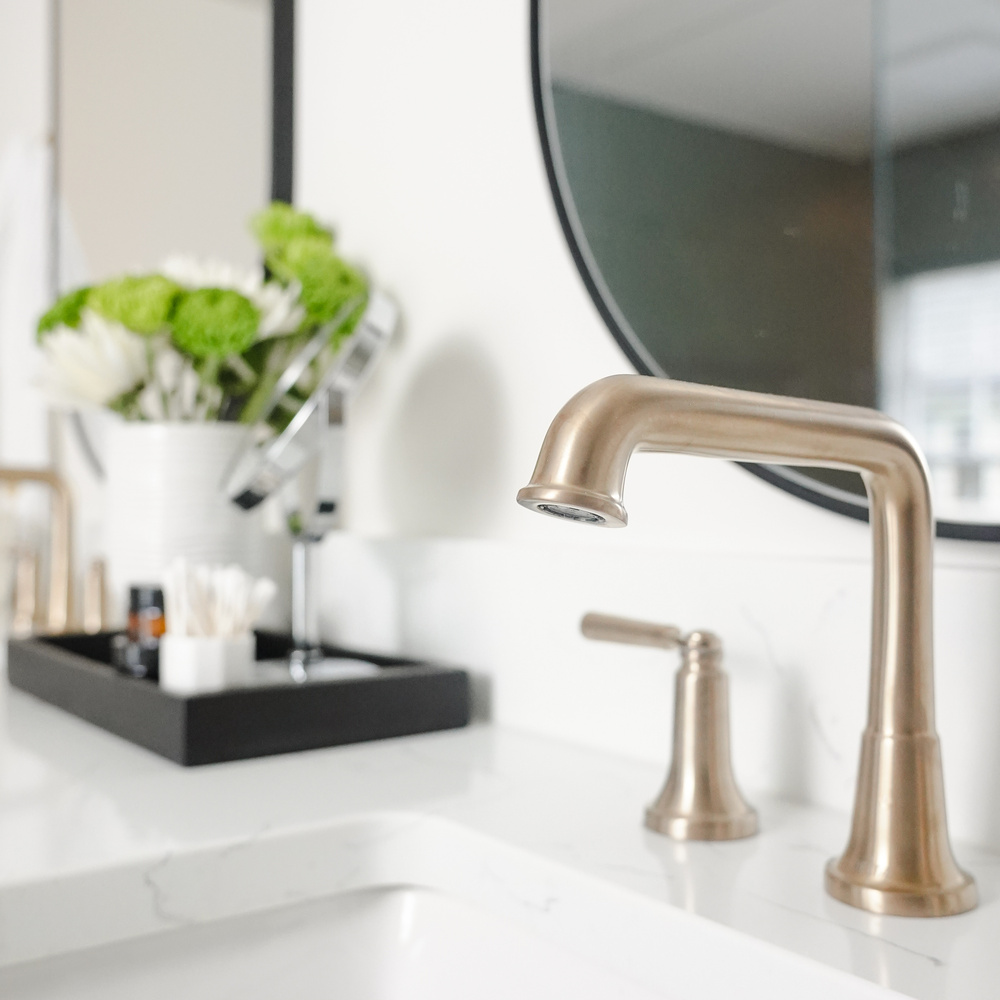 Modern vanity with brushed gold faucet and round mirror in a custom bathroom by Exodus Design Build in Braselton, GA.