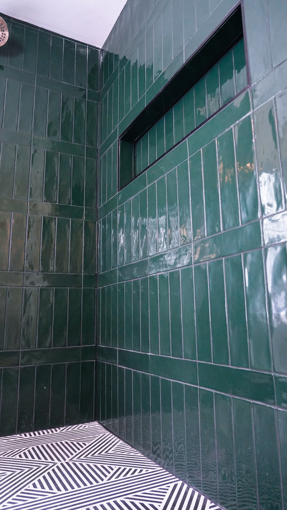 Vertical emerald green shower tiles with a recessed shelf designed by Exodus Design Build in a custom Lawrenceville, GA home.