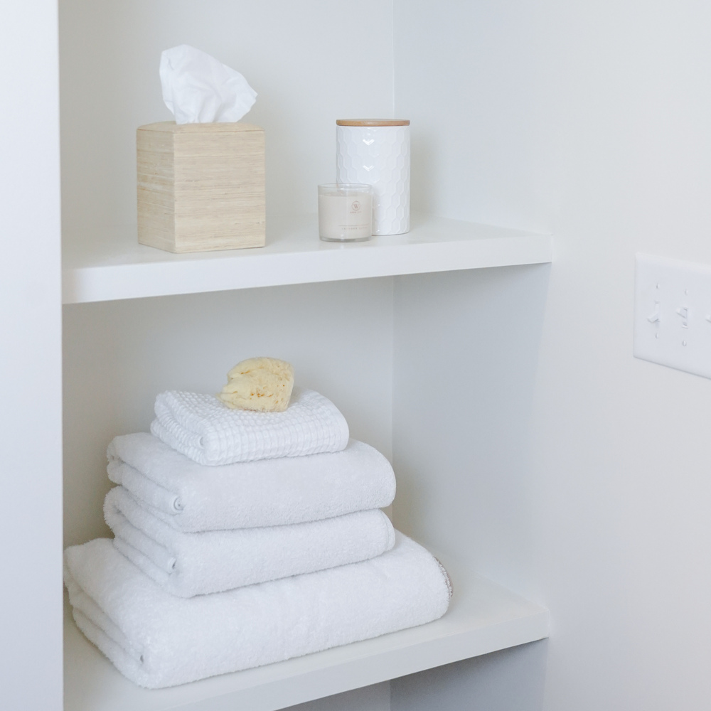 White open shelving with stacked towels and spa accessories in a custom home by Exodus Design Build in Gainesville, GA.