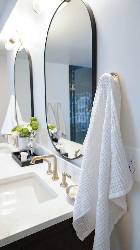 White towel hanging next to curved mirror over marble vanity by Exodus Design Build in Berkeley Lake, GA.