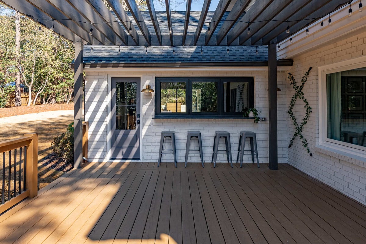 Backyard deck featuring modern bar window and string-lit pergola by Exodus Design Build in Berkeley Lake, GA