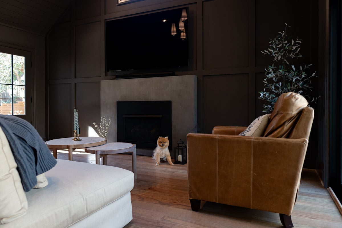 Living room with fireplace and leather armchair featuring a small dog by Exodus Design Build in Lawrenceville, GA