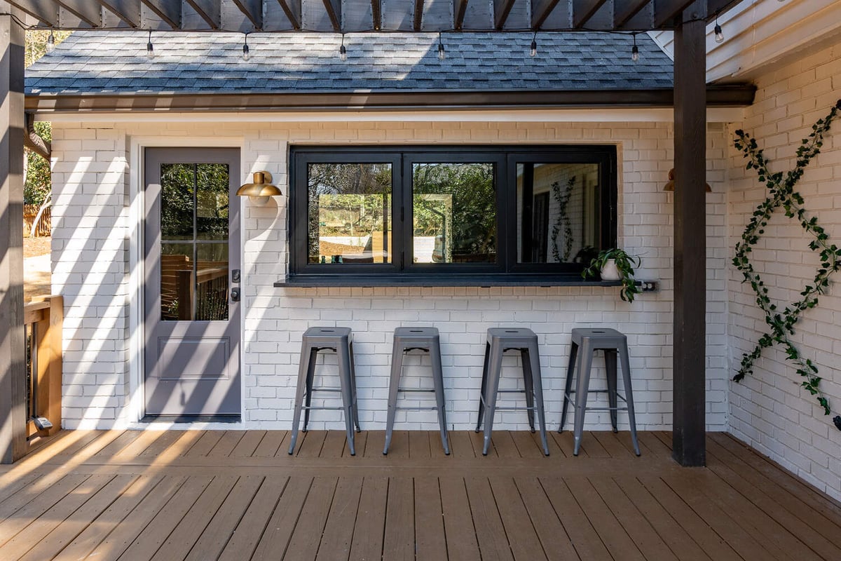 Outdoor bar seating area with white brick exterior and modern stools by Exodus Design Build in Johns Creek, GA