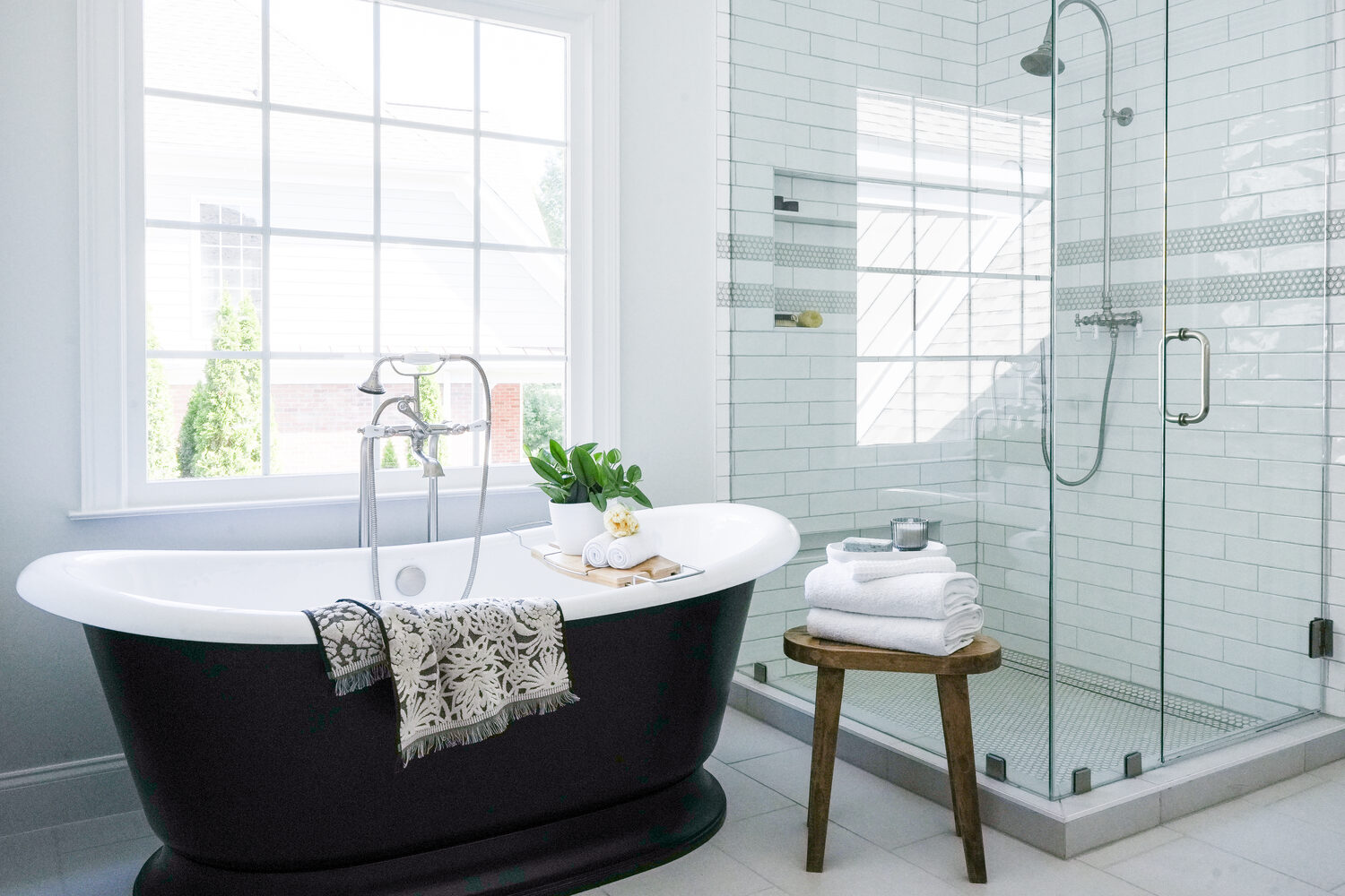 Freestanding black bathtub beside large window and glass shower in custom Atlanta bathroom by Exodus Design Build