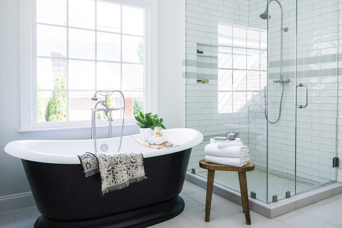 Freestanding black bathtub beside large window and glass shower in custom Atlanta bathroom by Exodus Design Build