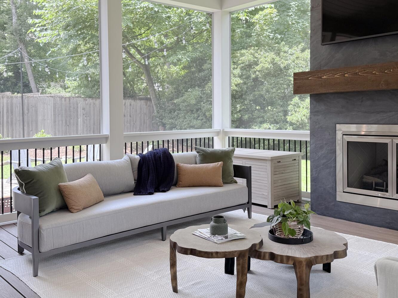 Stylish screened-in patio with modern sofa, wood coffee tables, and TV fireplace by Exodus Design Build in Johns Creek, GA.