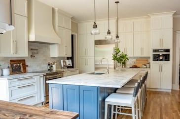 A renovated luxury kitchen with an island-centric layout, white cabinets, and marble countertops. 