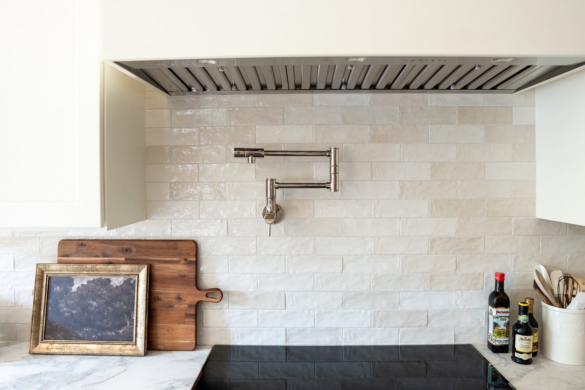 Stainless pot filler over marble backsplash and cooktop in Loganville, GA kitchen by Exodus Design Build.