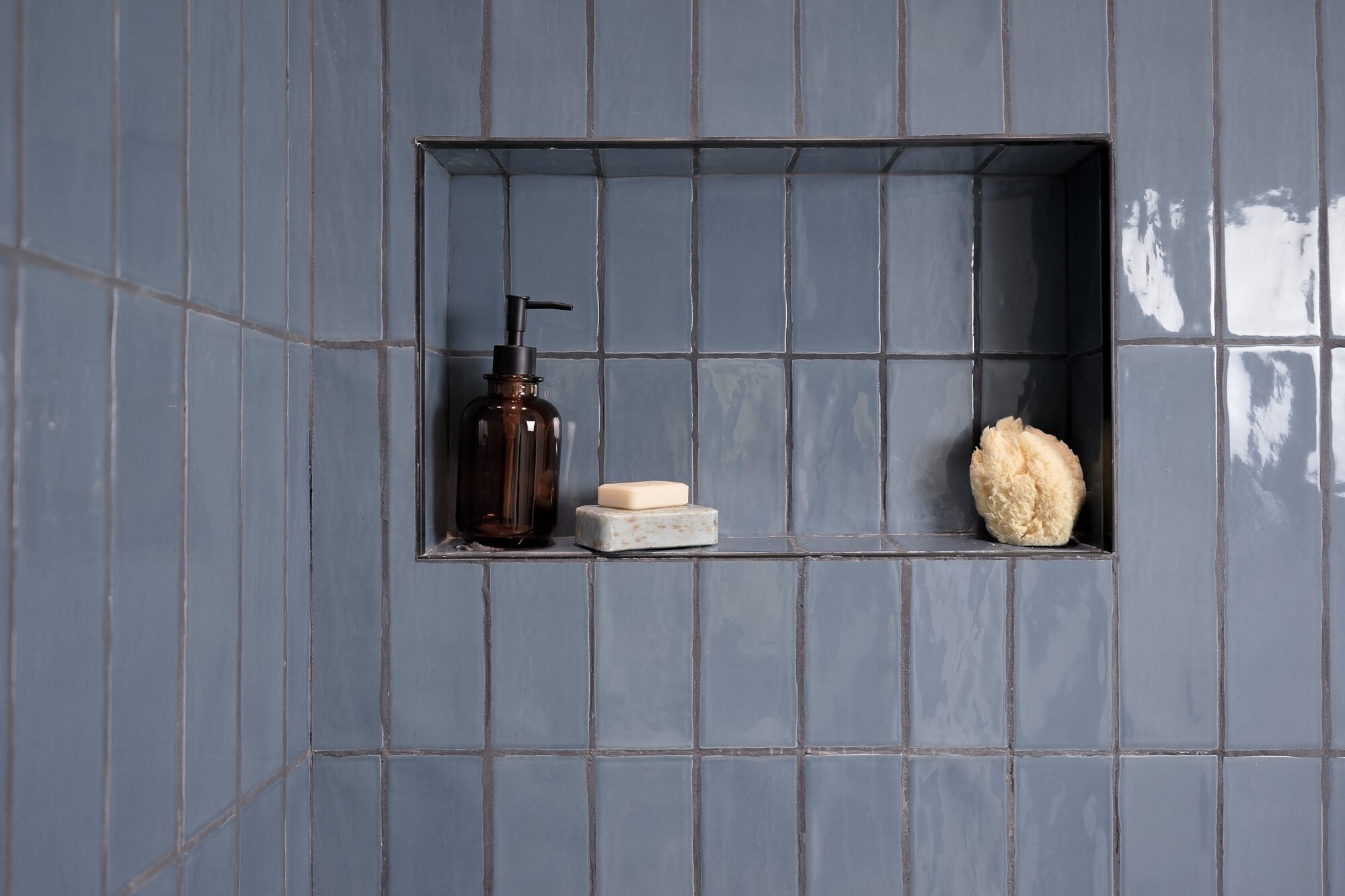 Blue shower niche with amber bottle, soap, and sponge in custom bathroom by Exodus Design Build in Oakwood, GA
