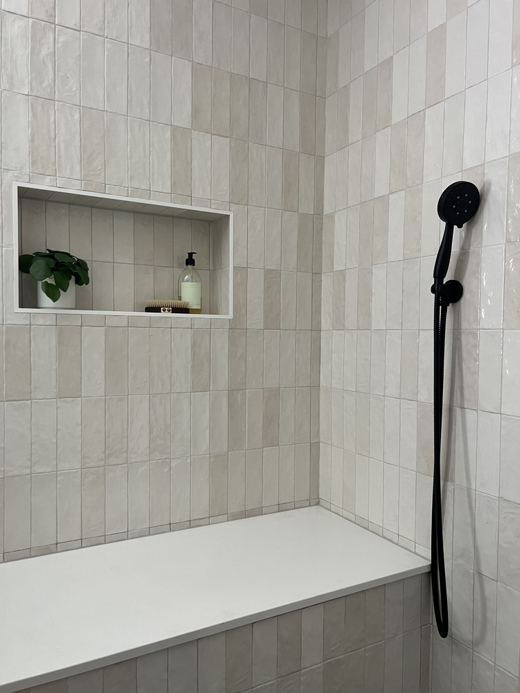 Tiled shower bench with built-in niche and black handheld sprayer in custom bathroom by Exodus Design Build in Loganville, GA.