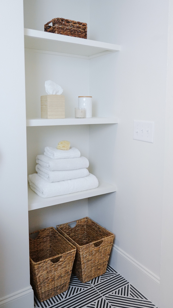 Built-in linen shelving with wicker baskets and neatly folded towels in a custom home bathroom by Exodus Design Build in Lawrenceville, GA.