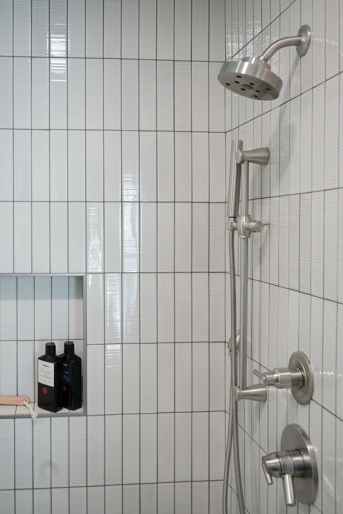 Stainless steel shower head and handheld sprayer in a vertical-tiled bathroom by Exodus Design Build in Stone Mountain, GA.