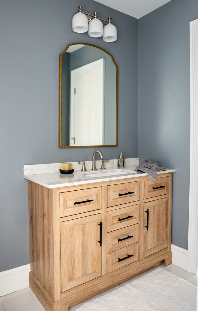 Vanity with marble countertop and curved gold mirror in Loganville, GA bathroom by Exodus Design Build