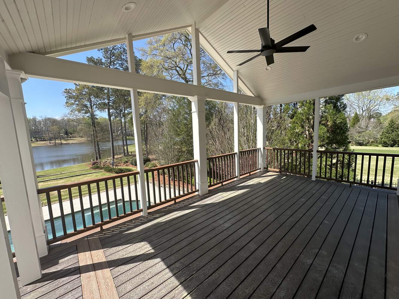 Open-air covered deck with wood railings and black ceiling fan by Exodus Design Build in Flowery Branch, GA.