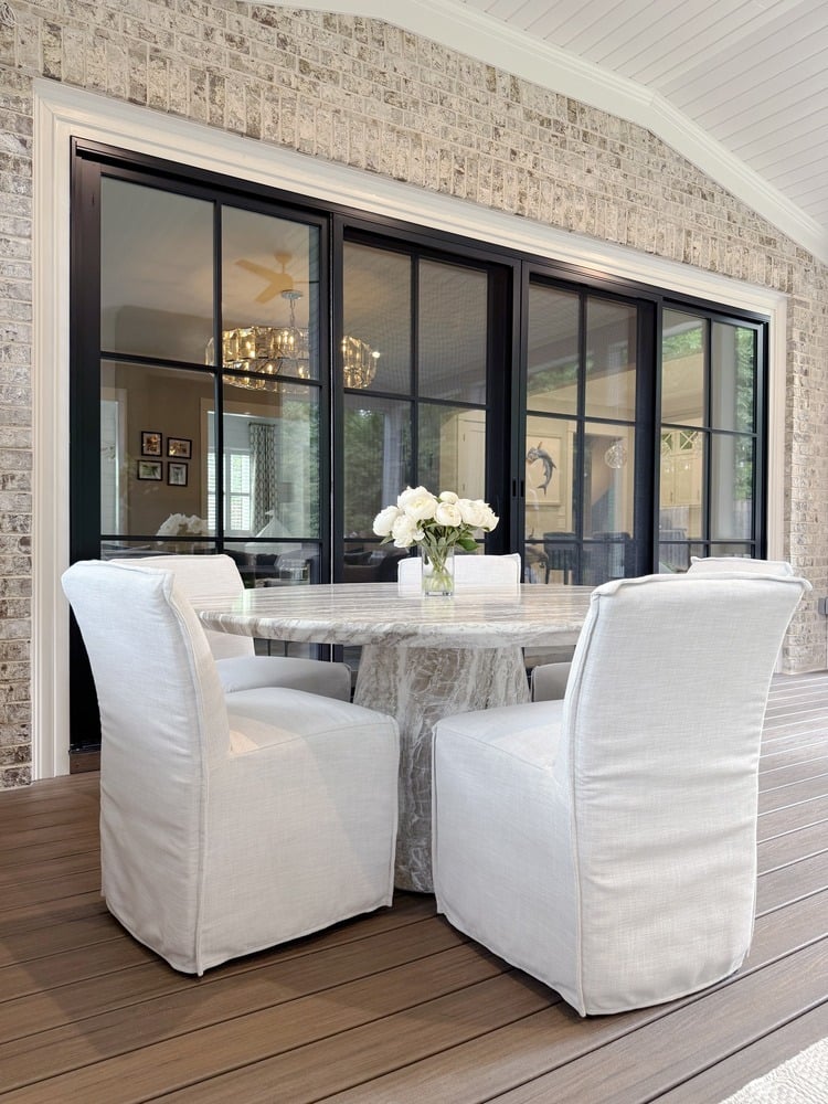 Screened-in porch dining area with white slipcovered chairs and round marble table by Exodus Design Build in Loganville, GA.